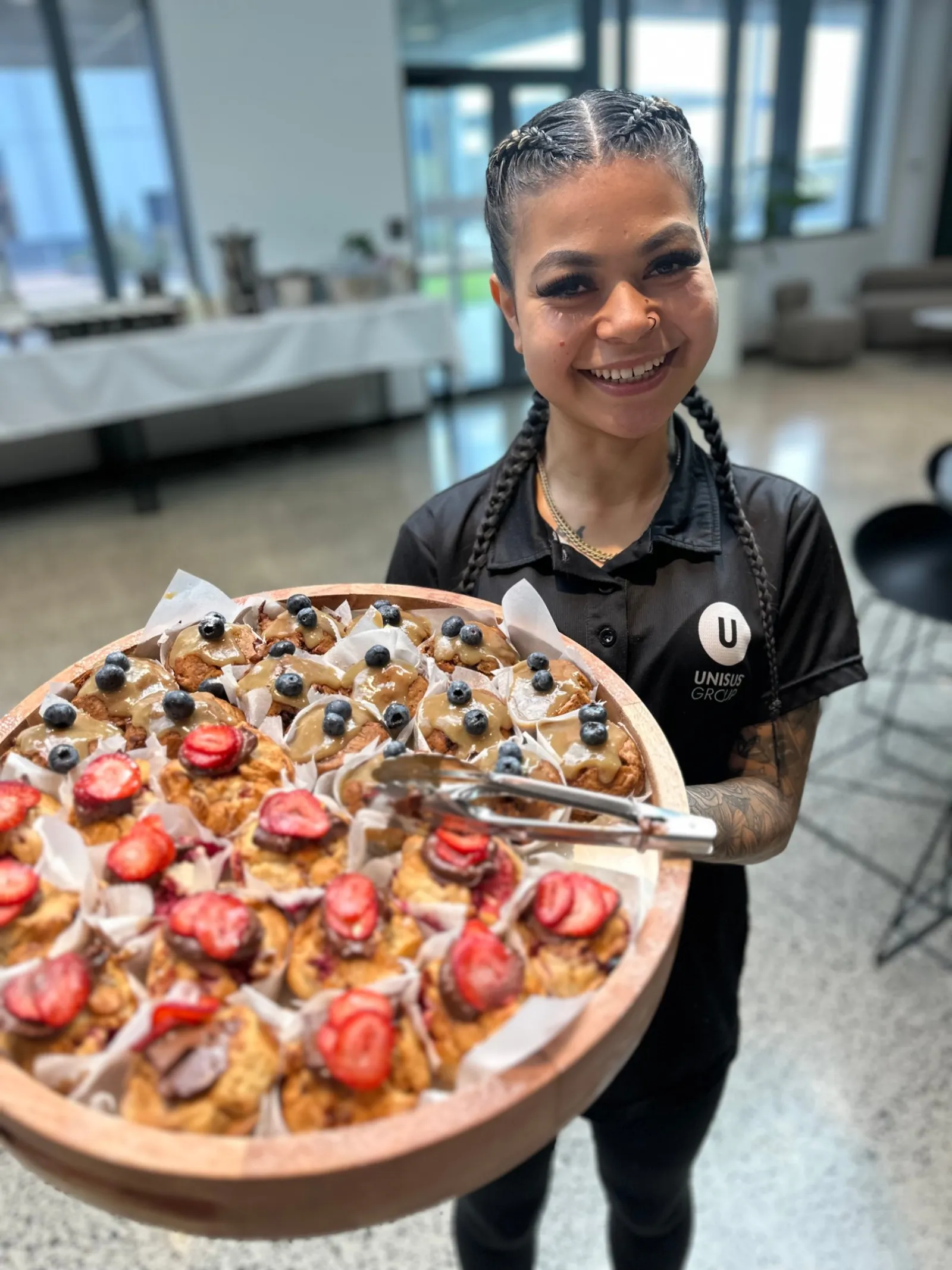 Smiling UNISUS team member presenting a platter of freshly baked berry muffins